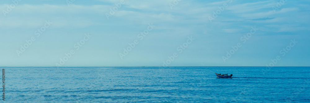 Simple background Calm dark blue sea fishing boat alone white pale Spindrift clouds Open way no limitations. BANNER LONG FORMAT