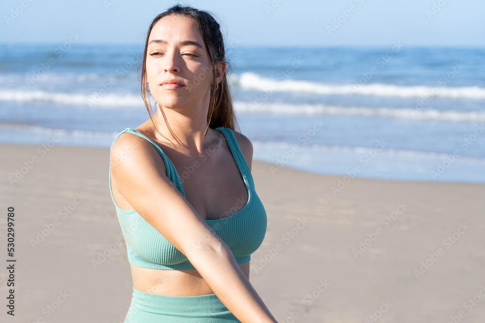 A young woman sitting on the shore of a lonely beach, she is stretching relaxed, breathing calm and self-confident. Concept of tranquility, confidence and security. A young woman sitting on the shore of a lonely beach, she is stretching relaxed, breathing calm and self-confident. Concept of tranquility, confidence and security.