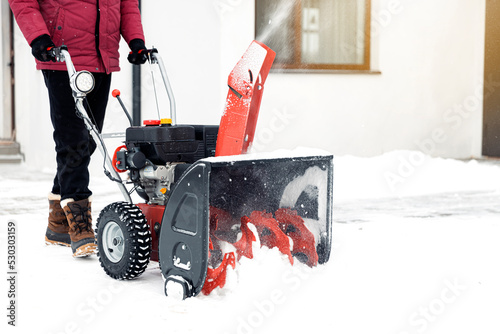 Closeup of red snow blower in action. Senior mature man outdoor in front of house using snowblower machine for removing snow on yard. Snow thrower in winter outside home. Young worker guy blowing snow photo