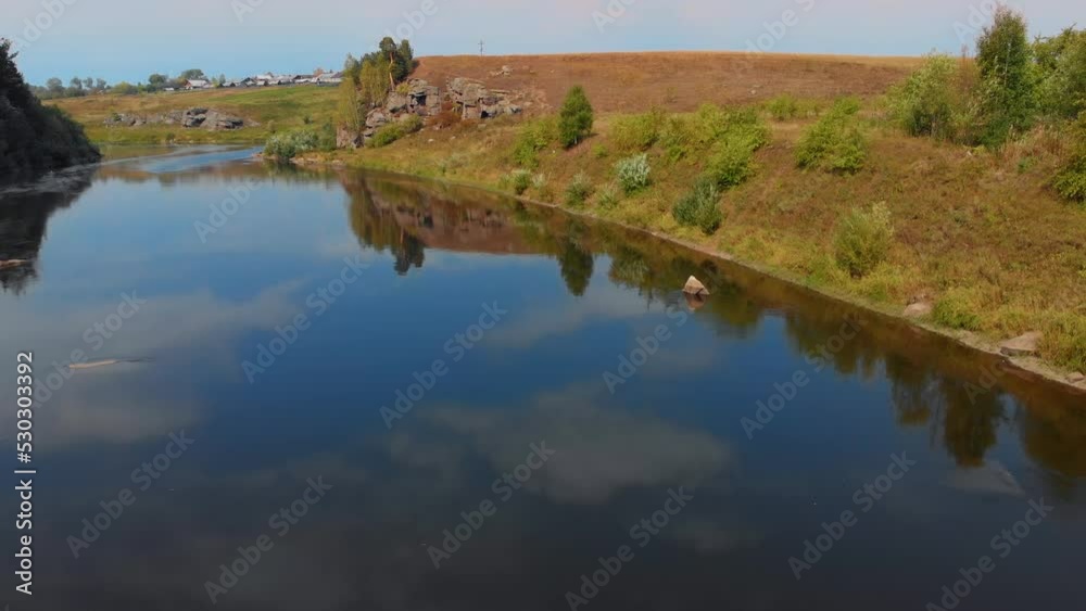 The drone flies over a calm river over which seagulls fly. Flight over the river with a view from the eyes of a bird, along the banks of the river there are rocks and a forest. The drone flies over a calm river over which seagulls fly. Flight over the river with a view from the eyes of a bird, along the banks of the river there are rocks and a forest.