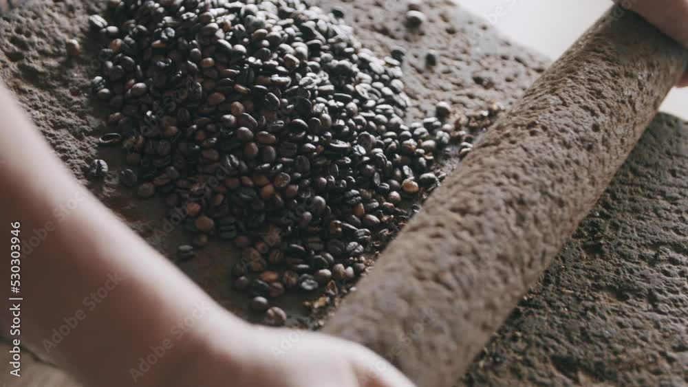 Slow motion footage of person just starting to grind coffee beans on a volcanic stone with a stone roll pin.