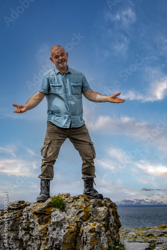 An elderly man on top of a rock on the seashore with a face expressing the joy of a climbing goal, Burren lanscape, Ireland