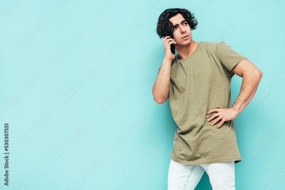 Portrait of handsome confident stylish hipster lambersexual model.Man dressed in over size T-shirt and jeans. Fashion male isolated in studio. Posing near blue wall. Talking at smartphone Portrait of handsome confident stylish hipster lambersexual model.Man dressed in over size T-shirt and jeans. Fashion male isolated in studio. Posing near blue wall. Talking at smartphone