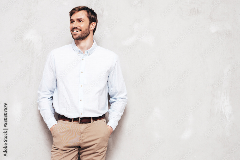 Portrait of handsome smiling model. Sexy stylish man dressed in shirt and trousers. Fashion hipster male posing near grey wall in studio Portrait of handsome smiling model. Sexy stylish man dressed in shirt and trousers. Fashion hipster male posing near grey wall in studio