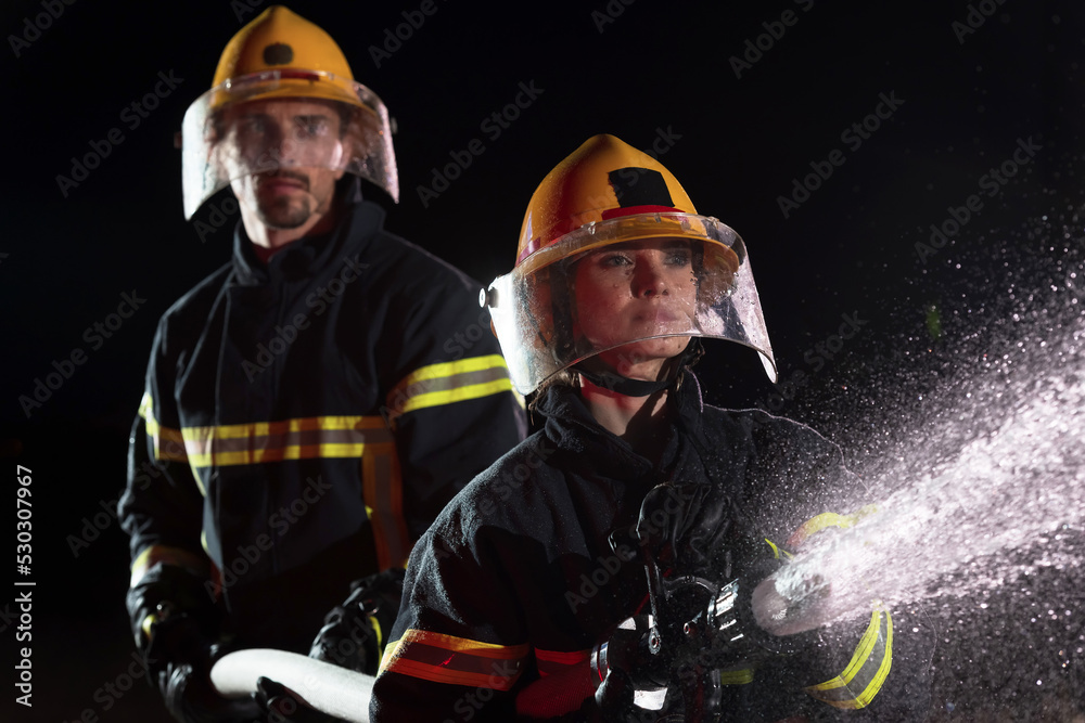 Fototapeta premium Firefighters using a water hose to eliminate a fire hazard. Team of female and male firemen in dangerous rescue mission. 