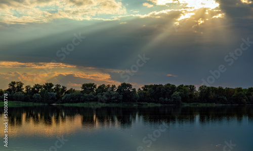 The bright rays of the Sun come out of the clouds over the river. Beautiful natural landscape of Ukraine in cloudy weather