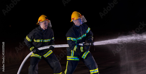 Firefighters use a water hose to eliminate a fire hazard. Team of firemen in the dangerous rescue mission.