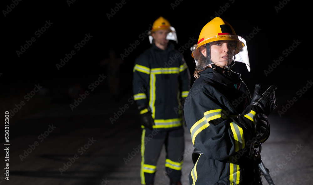 Firefighters using a water hose to eliminate a fire hazard. Team of female and male firemen in dangerous rescue mission. Firefighters using a water hose to eliminate a fire hazard. Team of female and male firemen in dangerous rescue mission.