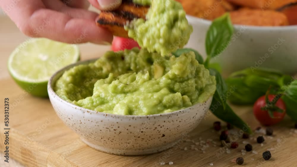 Sweet potato wedges and avocado sauce. Dipping potato fries into vegan avocado sauce, closeup view Sweet potato wedges and avocado sauce. Dipping potato fries into vegan avocado sauce, closeup view