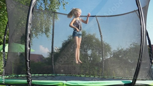 A cute little girl in a jeans shorts is jumping and having fun on the trampoline photo