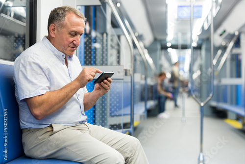 Elderly passenger is engrossed in information on smartphone while traveling in subway car