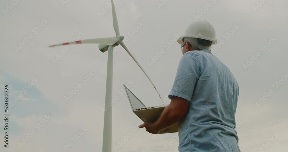 Engineer hardhat using laptop near wind turbines ecological energy electricity windmill renewable. Technician Engineer Wind Turbine Power Generator Station checks the status turbines using laptop Engineer hardhat using laptop near wind turbines ecological energy electricity windmill renewable. Technician Engineer Wind Turbine Power Generator Station checks the status turbines using laptop