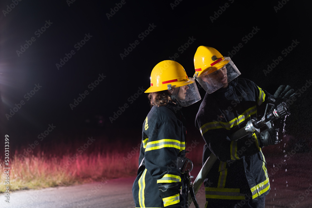 Firefighters using a water hose to eliminate a fire hazard. Team of female and male firemen in dangerous rescue mission. Firefighters using a water hose to eliminate a fire hazard. Team of female and male firemen in dangerous rescue mission.