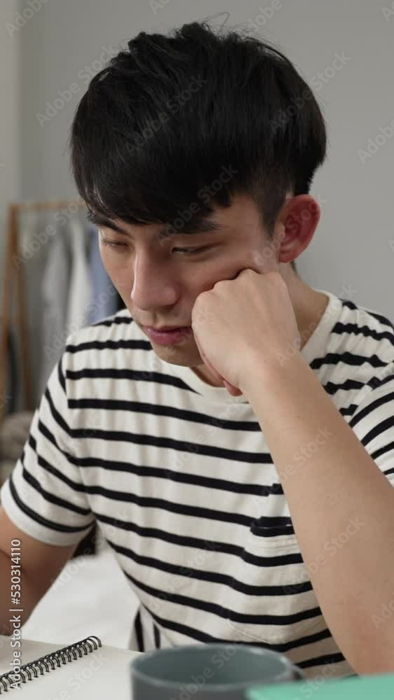Vertical Screen: sleepy korean young man holding pen and propping face is waking in shock as he falls asleep while learning from home on the laptop during covid19 quarantine. Vertical Screen: sleepy korean young man holding pen and propping face is waking in shock as he falls asleep while learning from home on the laptop during covid19 quarantine.