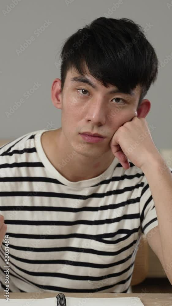 Vertical Screen: bored asian Korean male student staring at camera is propping head and playing with pen while learning from home watching a boring online lecture video in the bedroom Vertical Screen: bored asian Korean male student staring at camera is propping head and playing with pen while learning from home watching a boring online lecture video in the bedroom