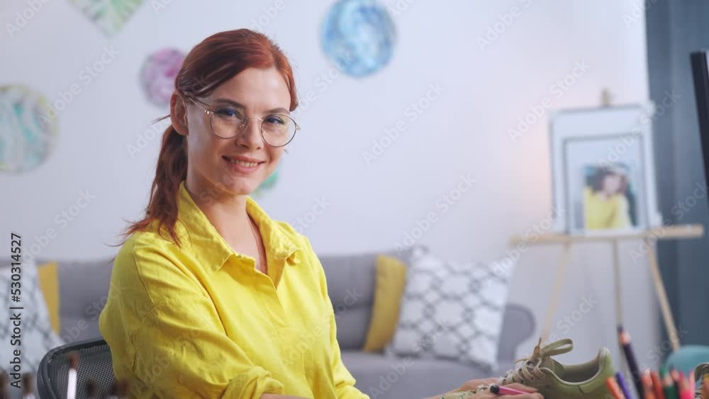portrait of a smiling creative female designer in glasses draws a print on worn sneakers with marker, rebrands following new fashion trends, smiles and looks at camera portrait of a smiling creative female designer in glasses draws a print on worn sneakers with marker, rebrands following new fashion trends, smiles and looks at camera