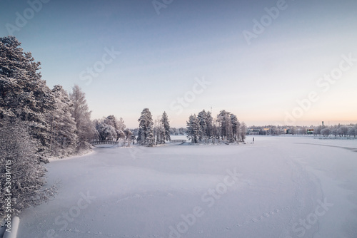 Frosty morning in the Finnish town of Kajaani in the north of the country in the Kainu region. A view of the frozen Kajaaninjoki river and the snowy forest near the river. Sunrise