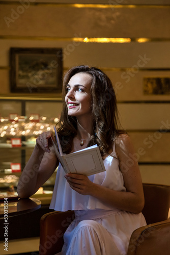 Diverse adult middle-aged woman sitting in cafe, smiling as she happily looks over menu options, thinking and looking away