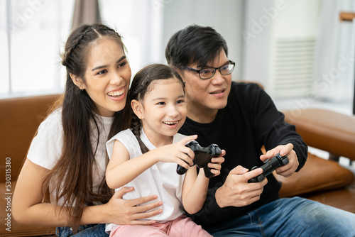 Family of Asian parents and daughters Spend your holidays together playing video games on the sofa in your house with fun and happy smiles.