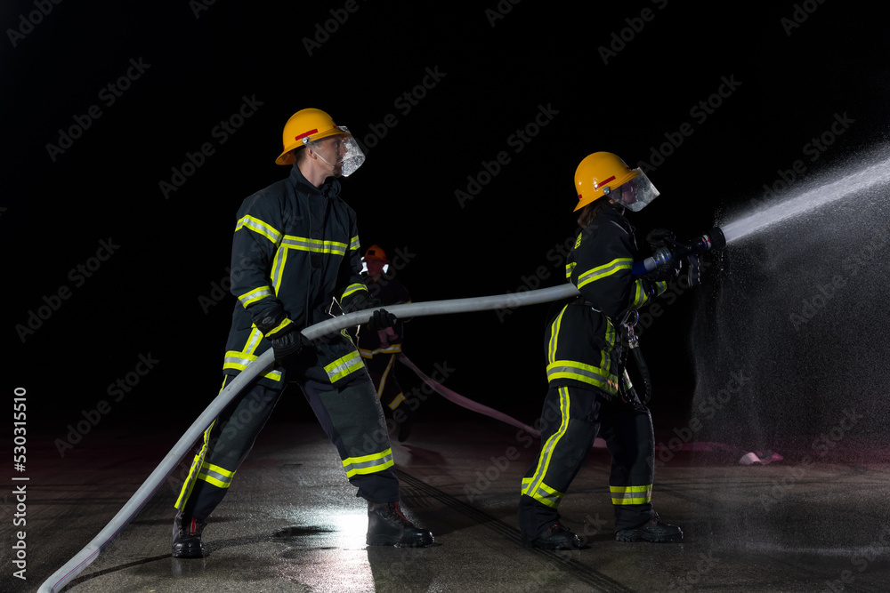 Firefighters using a water hose to eliminate a fire hazard. Team of female and male firemen in dangerous rescue mission. Firefighters using a water hose to eliminate a fire hazard. Team of female and male firemen in dangerous rescue mission.