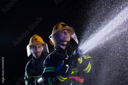 Firefighters using a water hose to eliminate a fire hazard. Team of female and male firemen in dangerous rescue mission. 