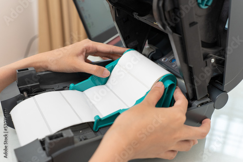 Asian woman inserts a barcode sticker into a barcode printer.