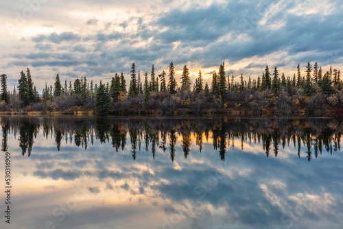 sunset over lake with reflection of coniferous trees in the water