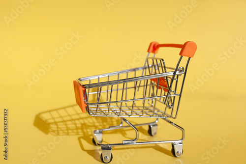 Small supermarket grocery push cart for shopping. Shopaholic. Buyer. Shopping concept. Close-up. Isolated shopping trolley on a yellow background. Copy space.