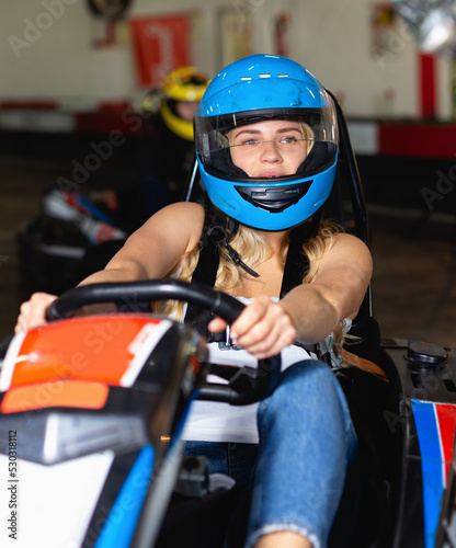 Cheerful positive girl and her friends competing on racing cars at kart circuit
