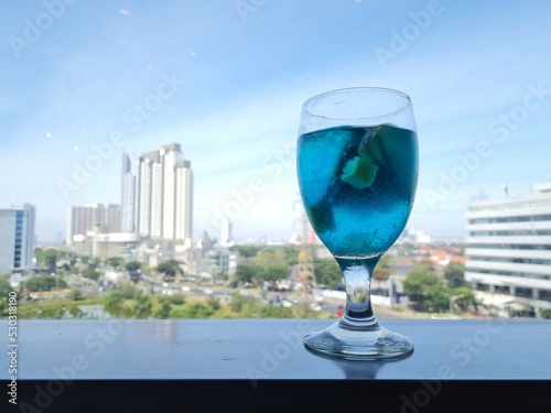 Closeup glass of blue lagoon cocktail decorated with lime on glass window background and city view. the concept of thirst while living in the city