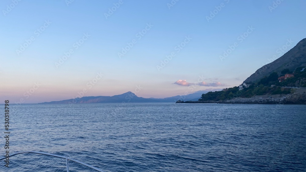 Landscape of the south of Italy from a boat at sunset with high hills, sea till the line of the horizon with past colour in a sunny day