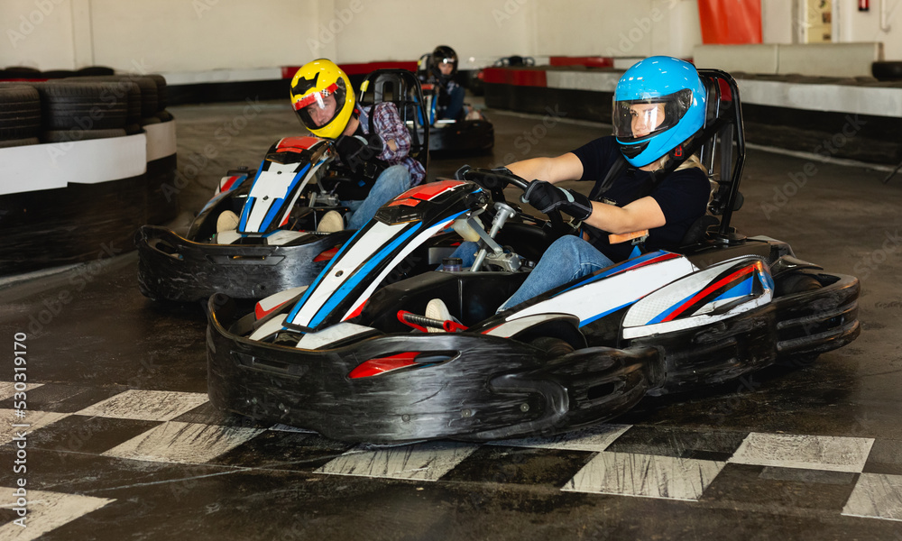 Young positive people in helmets driving go-kart cars in karting club