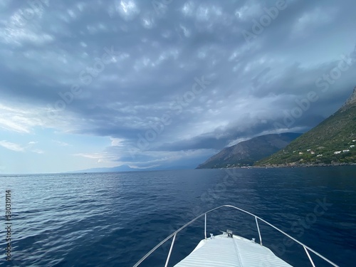 Landscape of the south of Italy from a boat at sunset with high hills, sea till the line of the horizon just before a storm, cloudy sky reflecting on the sea © BC-Consulting