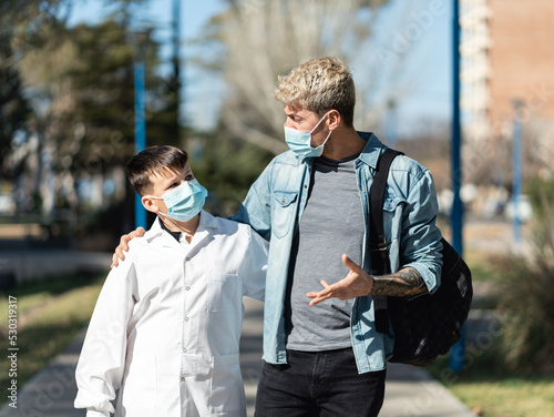 Father and son walking to school wearing face mask and a white smock (an Argentinian white coat for public schools). photo