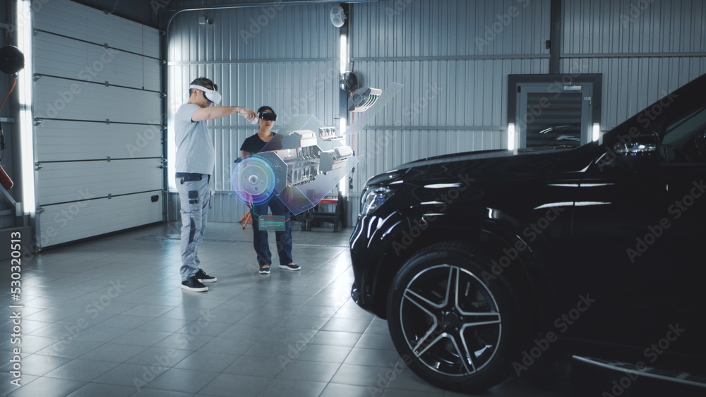 Two technicians check a car engine using virtual reality technology in a workshop. Experts discuss the characteristics of the motor of the car, its components and parts Two technicians check a car engine using virtual reality technology in a workshop. Experts discuss the characteristics of the motor of the car, its components and parts