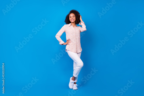 Full size photo of charming gorgeous lady put arm waist touch curly hairstyle isolated on blue color background