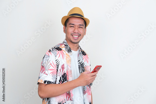 Asian man wearing beach shirt smiling happy while holding mobile phone photo