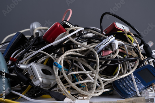 Pile of tangled old smart technology wires, charging cables and used obsolete mobile phones. Old electronic devices. The concept of recycling and disposal of electronic waste.