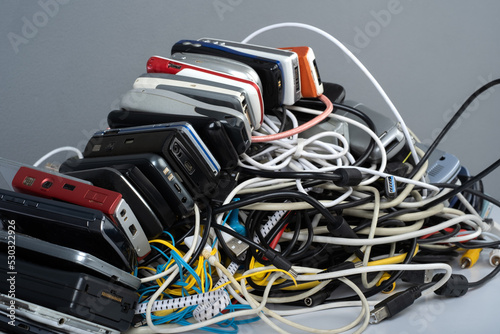 Pile of tangled old smart technology wires, charging cables and used obsolete mobile phones. Old electronic devices. The concept of recycling and disposal of electronic waste.