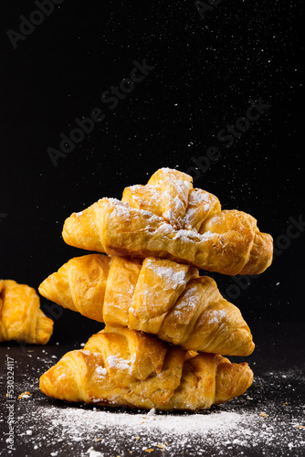 Vertical image of croissants with powder sugar on black background