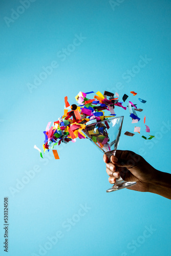 Composition of close up of hand with new years drink with confetti on blue background