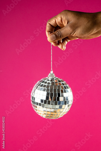Composition of close up of hand with new years bauble on pink background