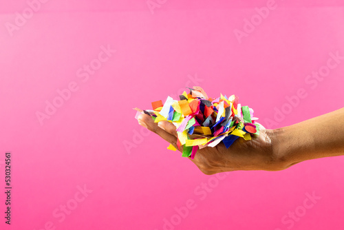 Composition of close up of hand with new years confetti on pink background