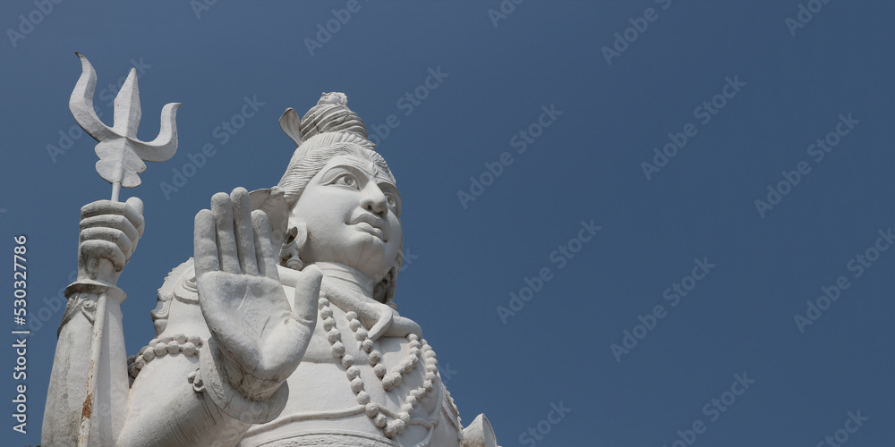 Four-armed Lord Shiva with a trident and a cobra around his neck. Lord Shiva blesses with a gesture. Giant statue in India. Angle from bottom to top.