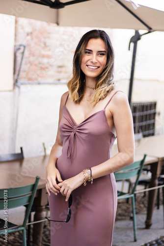 Young Italian woman in casual simple dress staying , looking and smiling in restaurant outdoors