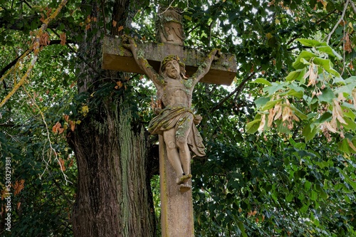 Mystische Ort - Altes steinernes Kruzifix unter einem schattigen Baum