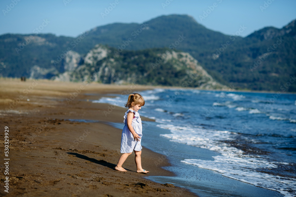 Cute little toddler girl in blue dress runnig and playing on the wild Iztuzu beach, Turkey Cute little toddler girl in blue dress runnig and playing on the wild Iztuzu beach, Turkey