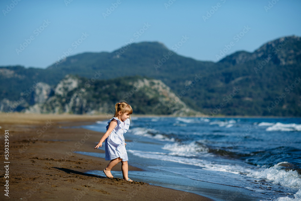 Cute little toddler girl in blue dress runnig and playing on the wild Iztuzu beach, Turkey