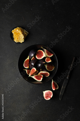 Fresh figs in pieces with honey in a black bowl on a black background
