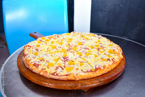 Pizza hawaiana con queso y jamón sobre una mesa de un restaurante photo